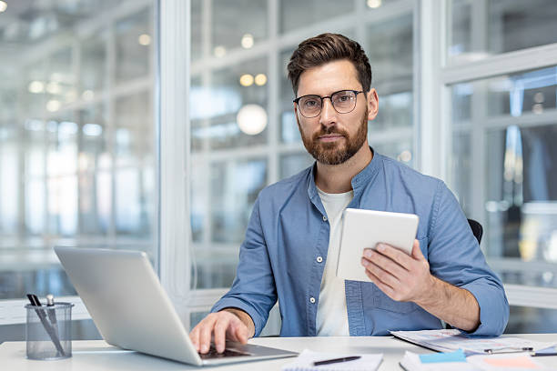istock Professional man working on laptop holding tablet in modern office 2256053171