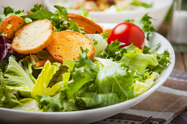 A small side salad with mixed greens, cherry tomatoes, balsamic dressing and a slice of bread served in a white bowl.
