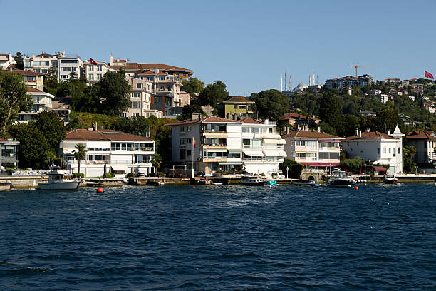 Istanbul, Turkey-January 24, 2026: A daytime view of multi-story luxury residential buildings and historical mansions built on the hills along the Bosphorus strait, with small motorboats moored at the shoreline in Istanbul, Turkey.