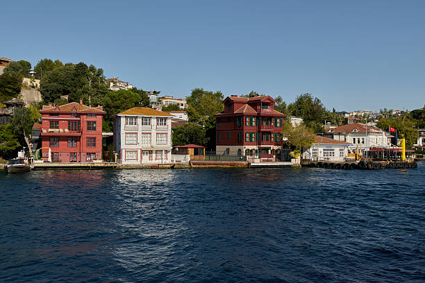 Istanbul, Turkey-January 24, 2026: A panoramic view of the Asian shoreline of the Bosphorus in Istanbul, Turkey. The image showcases a row of traditional red and white wooden waterfront mansions (Yalis) alongside the historic Cengelkoy ferry terminal, set against a lush green hillside and the deep blue waters of the strait.