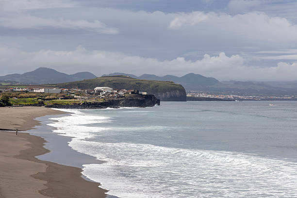 A beach with a rocky shoreline and a cloudy sky. The beach is empty and the waves are small