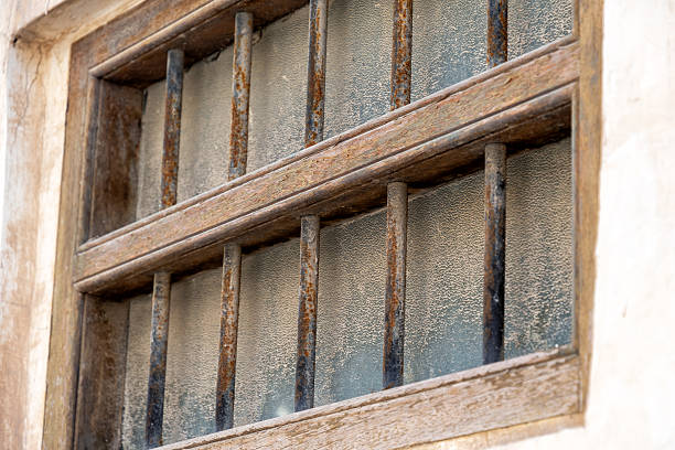 Close-up of an old, weathered window with rusty metal bars and textured frosted glass. Evokes themes of confinement, history, and decay