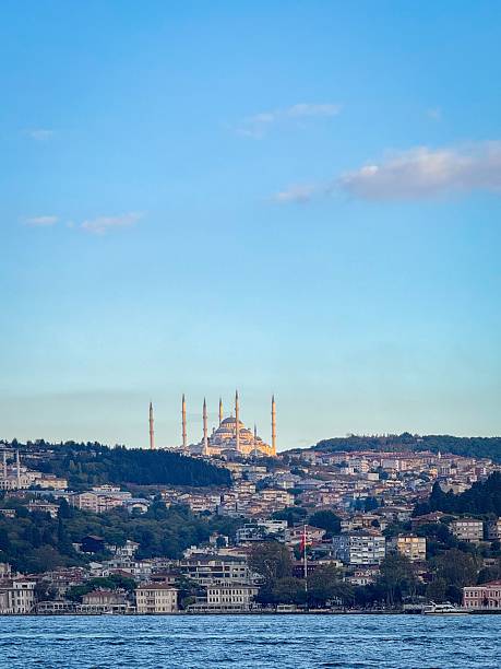 Scenic view across the Bosphorus toward Istanbul's Asian side, with the landmark Grand Camlica Mosque rising above the skyline, small boats on choppy water under a lightly clouded sky in Turkey