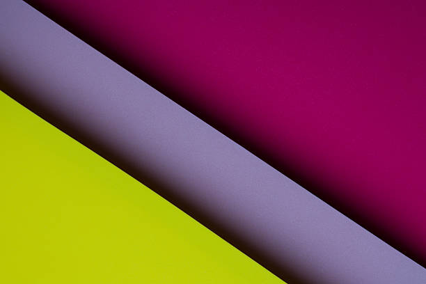 Bright sheets of paper are placed diagonally on a flat surface. The colors include purple, magenta, and yellow, creating a vibrant visual effect for crafting.