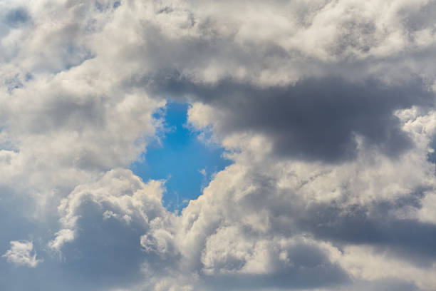 Clouds with a diamond-shaped gap revealing a blue sky on a bright day, showcasing the complexity of natural structures in close-up.