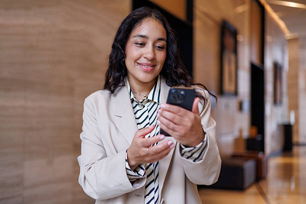 istock Professional woman smiling, using smartphone for communication and networking in modern office hotel lobby 2256075245