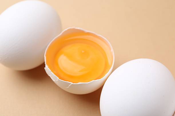 Whole and broken chicken eggs on beige background, closeup
