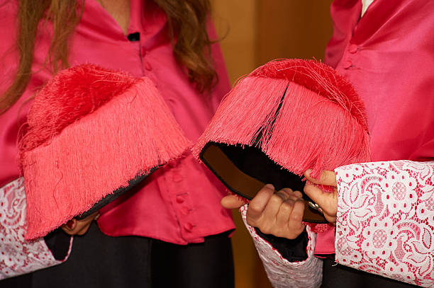 People wearing academic dress and holding traditional birretas with red tassels and lace cuffs during a graduation ceremony