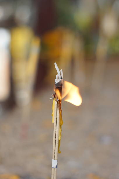 Close-up of a burning incense stick with visible flame, sharp focus on the subject and blurred background, symbolizing spirituality, ritual, meditation, and faith.