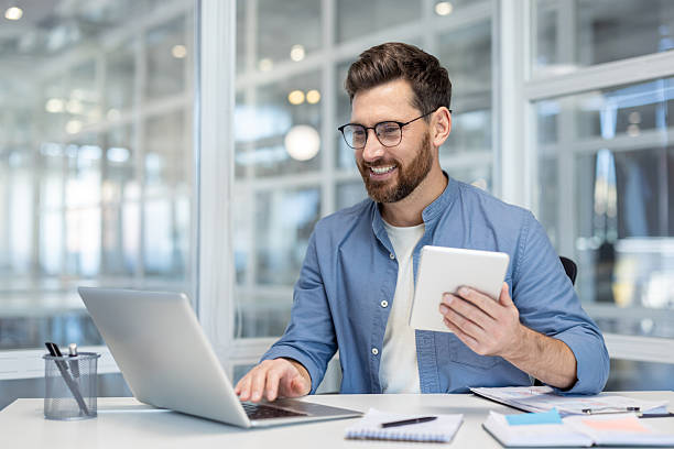 istock Happy businessman working on laptop and holding tablet 2256084403