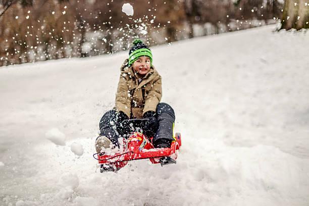 Happy boy sledding downhill on a snow-covered hill, kicking up a spray of powder as he speeds down, smiling with pure winter joy and carefree outdoor fun