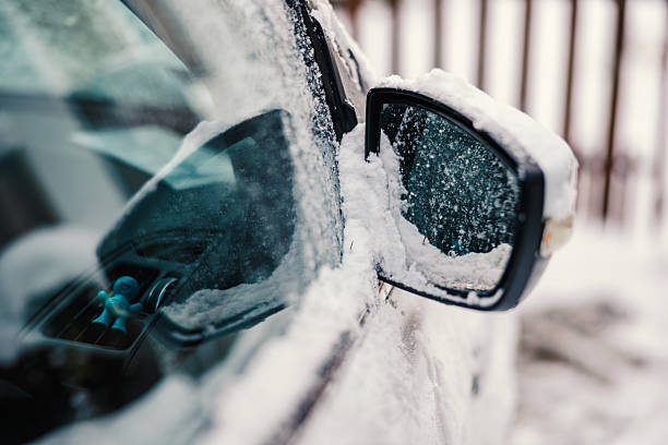Car side mirror completely covered in fresh snow and ice, frosty texture and frozen reflection signaling winter driving hazards, low visibility and cold outdoor conditions