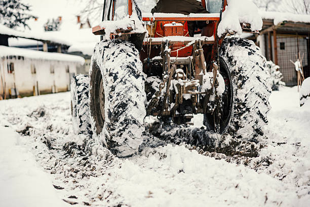 Agricultural tractor driving through snow and mud, leaving deep tracks in the rural landscape on a frosty day, representing hard work and resilience during cold seasons