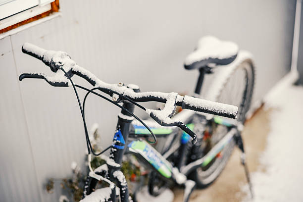 Bicycle handlebars and seat are covered in fresh white snow, standing outdoors on a chilly day, symbolizing the arrival of winter weather and a pause in cycling activity