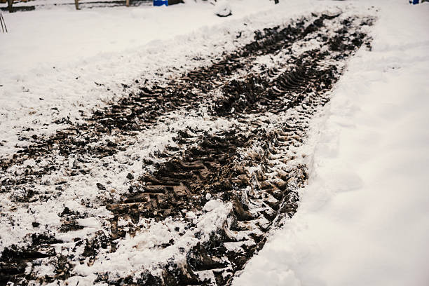 Heavy vehicle tire tracks slash through melting snow and mud, forming deep ruts and slushy, dirty patterns across a desolate rural road in late winter thaw