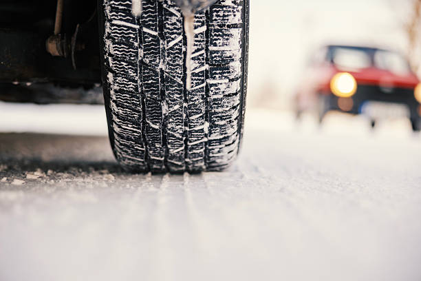 Macro shot of a winter tire tread covered in snow. Detailed view of rubber sipes and grip pattern on an icy road, emphasizing automotive safety, traction, and seasonal vehicle maintenance