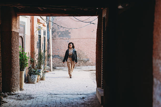 Young adult woman walking through a narrow alleyway in the Medina of Marrakech, exploring the historic urban environment