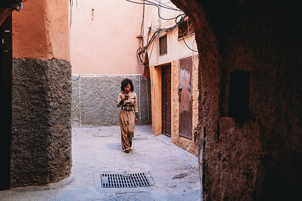 Young adult woman walking while concentrating on her smartphone in a narrow alley of the Marrakech Medina
