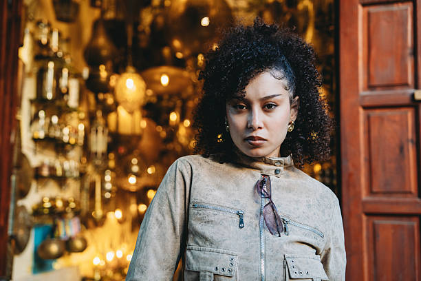 Young adult woman with curly hair exploring a traditional souk, wearing a jacket and sunglasses in Marrakech, Morocco
