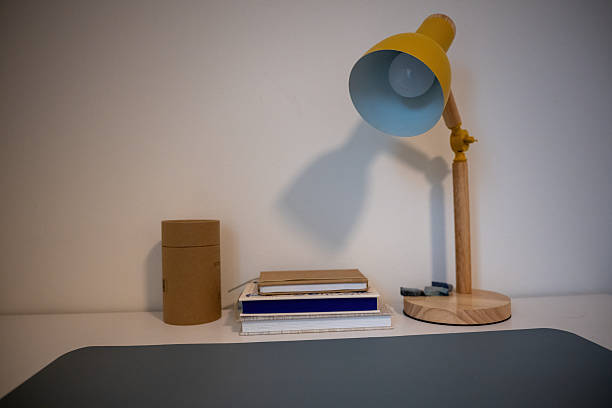 home workspace with colorful desk lamp notebooks and cardboard storage on clean white shelf