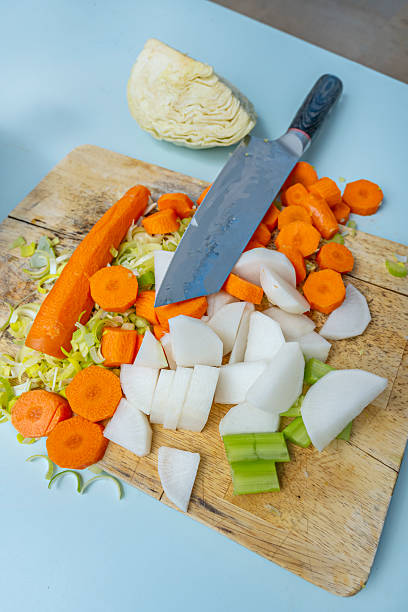Process of cutting vegetables for stew, where the turnips, carrots, and chives create a chromatic contrast on the light wood board