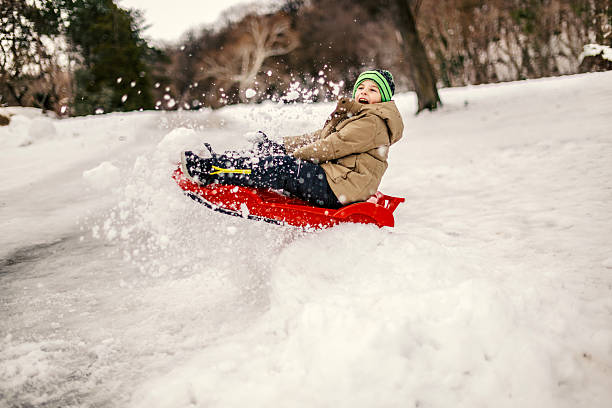 Young boy smiles with joy and splashes snow while rapidly sledding down a snowy hill, experiencing the exhilaration and fun of winter sports and outdoor play