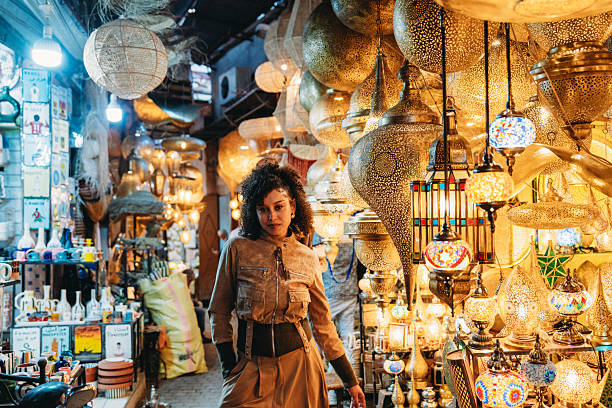 Young woman standing amidst many hanging metal lanterns in a vibrant traditional market in Marrakech, Morocco
