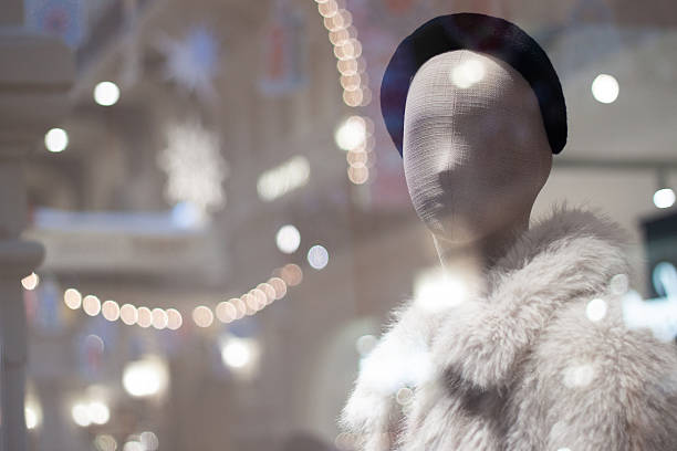 Shop window with a female mannequin in a white fur coat and a black hat. The window reflects the glare from the lamps and garlands.