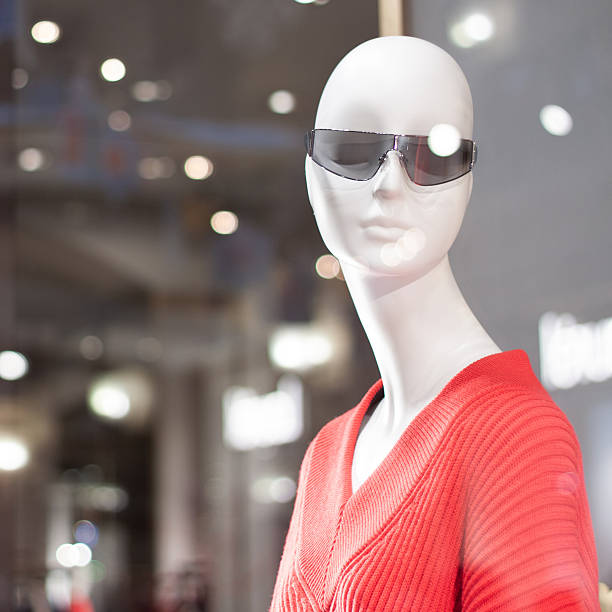Shop window with a female mannequin with a graceful long neck in a red blouse. The window reflects the glare from the lamps and garlands.