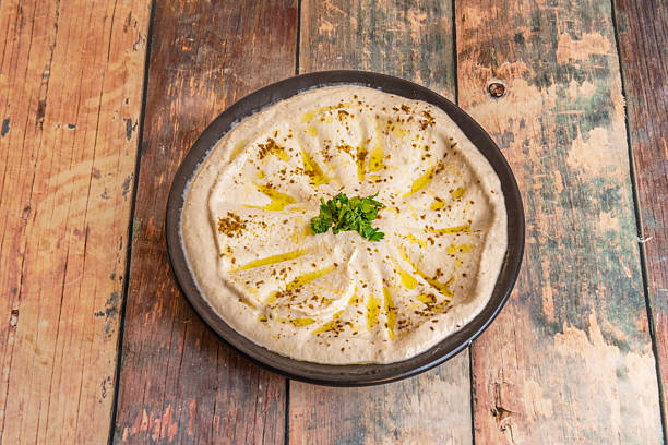 A plate of hummus artistically decorated with ingredients arranged in concentric circles: oil, paprika, cumin, and chopped parsley