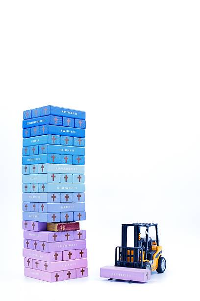 Wonderful multi color tower of wooden blocks with Bible references printer on the side of the blocks. Old Bible in Gap of the tower. Forklift carrying one block.