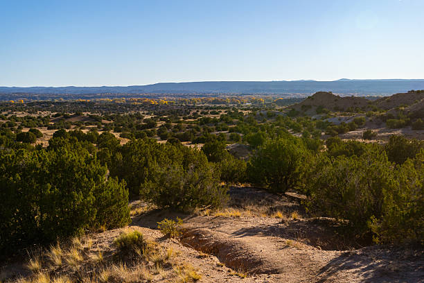 The Nambe Badlands glow under a warm golden hour light in New Mexico. Eroded sandstone formations and winding trails offer dramatic views toward the majestic Sangre de Cristo Mountains.
