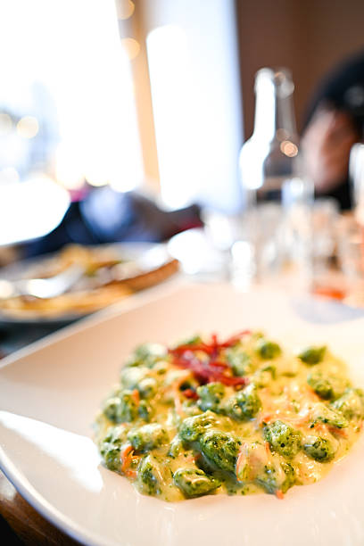 Green spinach gnocchi in a creamy yellow sauce topped with red garnish on a white plate