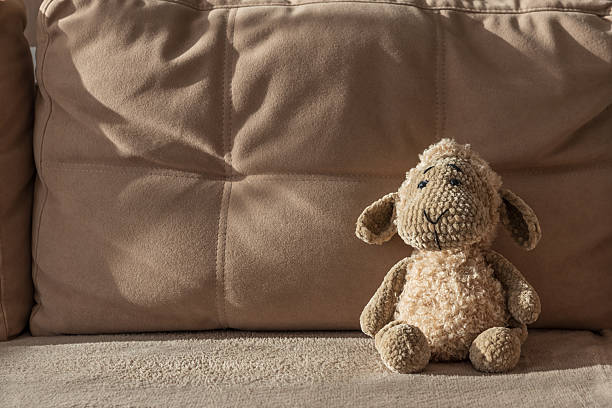A handmade soft toy in the shape of a white sheep peeks out from behind a blue wall with space for your text. High quality photo