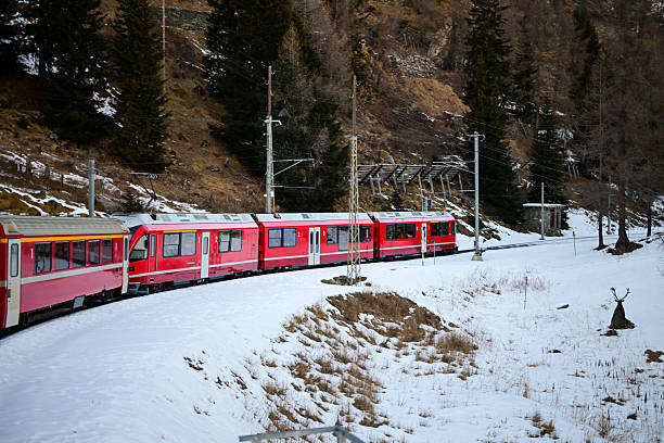 Red train moving through a winter landscape with snow-covered ground and mountains
