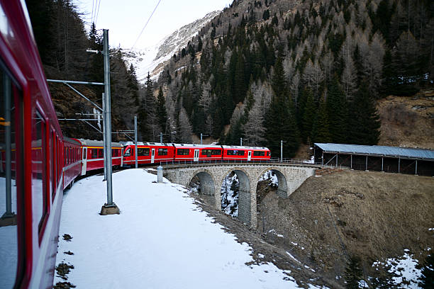Red train traveling on a stone arch bridge through a snowy mountain landscape
