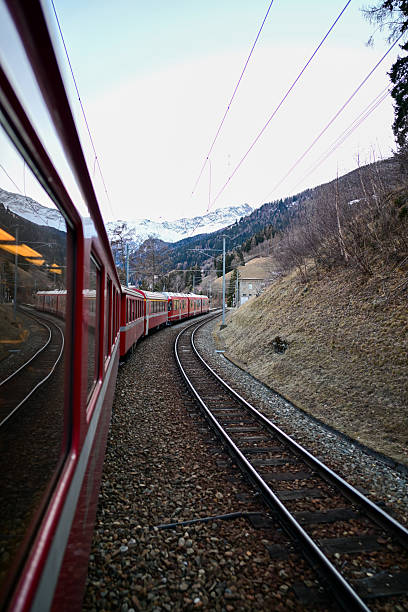 Red train navigating a curved track with snow-capped mountains in a scenic valley