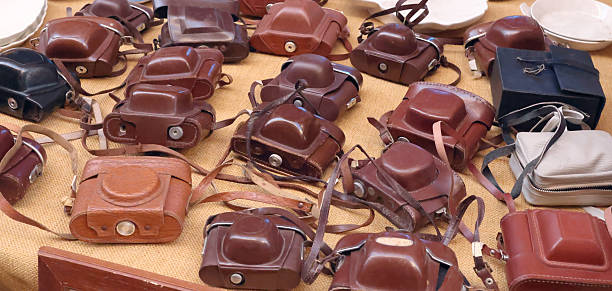 Vintage Leather Cameras on Market Stall. Assortment of old leather-cased analog cameras on yellow fabric at antiques market, retro textures and nostalgia.