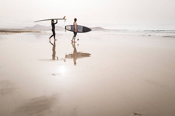 istock Female Surfers Carrying Surfboards Along Sandy Beach 2256115841