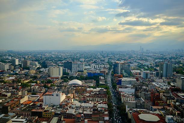 A wide panoramic view of Mexico City shows a long straight avenue stretching toward the distant mountains.