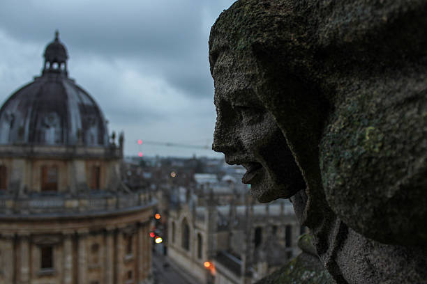 Oxford, United Kingdom - Dec 22, 2025: A view of the iconic Radcliffe Camera in Oxford, England, framed by a stone gargoyle from the University Church of St Mary the Virgin on a cloudy day.