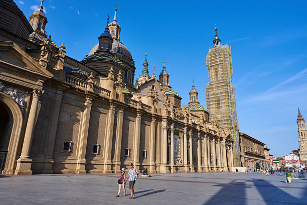 Zaragoza, Spain - June 12, 2025: a tourist couple walking past the Cathedral-Basilica of Our Lady of the Pillar, locally known as Catedral-Basílica de Nuestra Señora del Pilar.