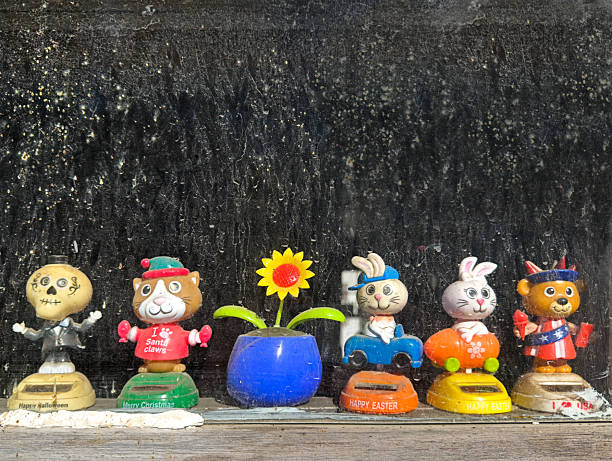 A row of six bobblehead toys line the sill of a dirty old window.
