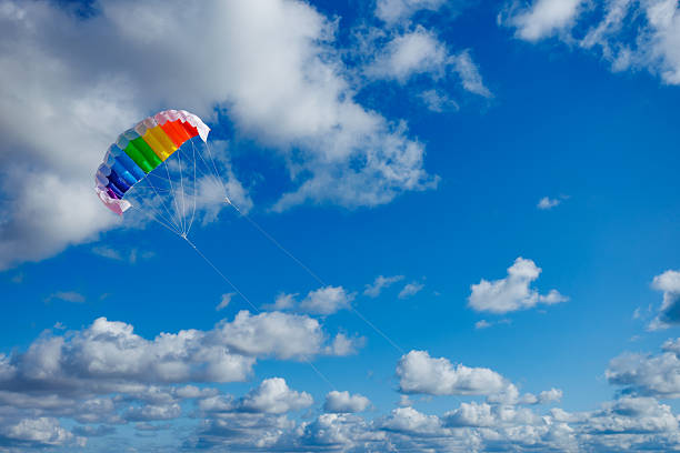 A vibrant rainbow-colored parachute is flying high against a backdrop of fluffy white clouds, showcasing the thrill of outdoor adventure and exciting sports activities in nature