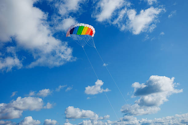 A vibrant rainbow parachute gracefully ascends into the blue sky, surrounded by fluffy white clouds, capturing the essence of adventure and the thrill of outdoor activities