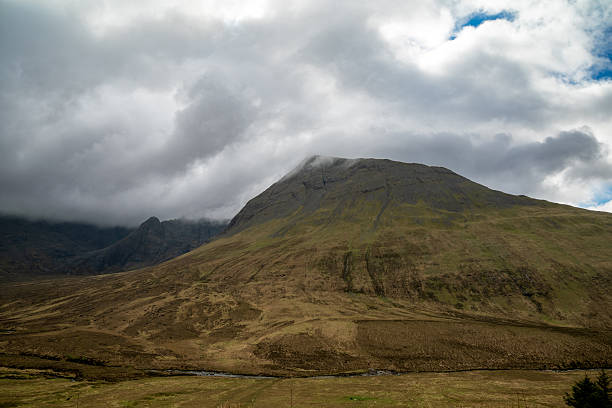 A wide vista of the rugged Glen Brittle valley under a heavy overcast sky, showcasing the vast scale of the Isle of Skye.
