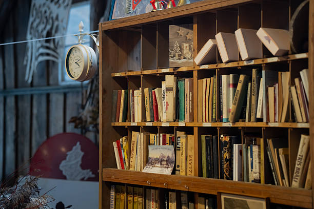 ustic wooden bookcase packed with old books and small postcards, warm indoor library corner with hanging wall clock and workshop backdrop in soft light
