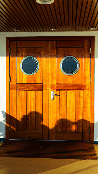 Wooden door with portholes on a cruise ship deck catching warm sunlight with people shadows