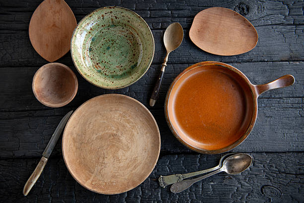 Top view flat lay of rustic ceramic dishes, wooden boards and vintage cutlery arranged on a dark wooden table.