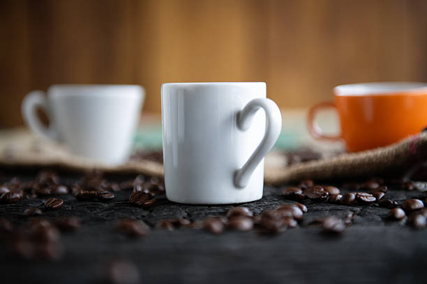 Group of ceramic coffee cups surrounded by roasted coffee beans on a warm wooden background.